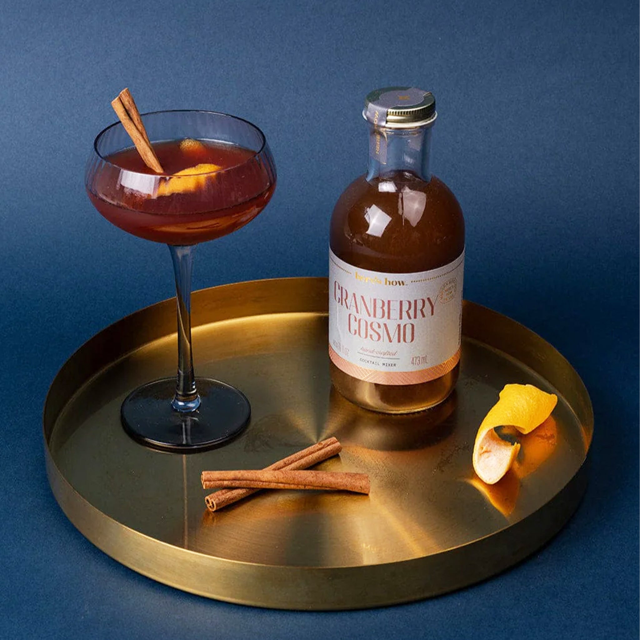 A glass bottle of Cranberry Cosmo with a blue label and gold lid. 