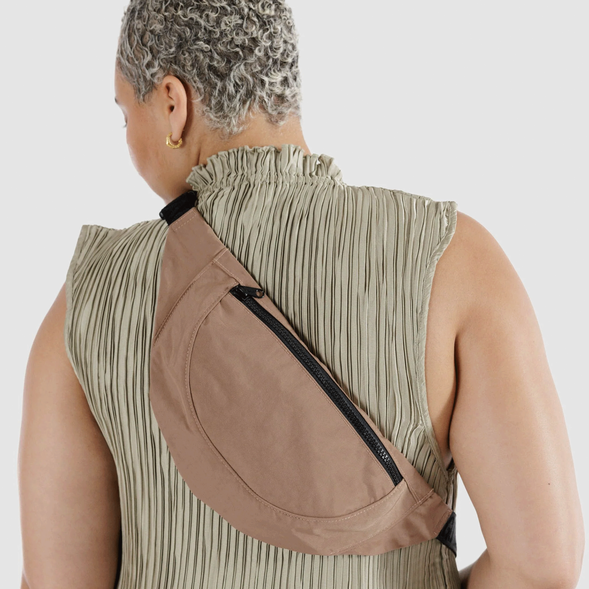 On a white background is a model wearing a light brown fanny pack with black details.
