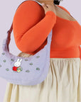 A light blue / lavender crescent bag with a Muffy and floral embroidered print and adjustable strap. 