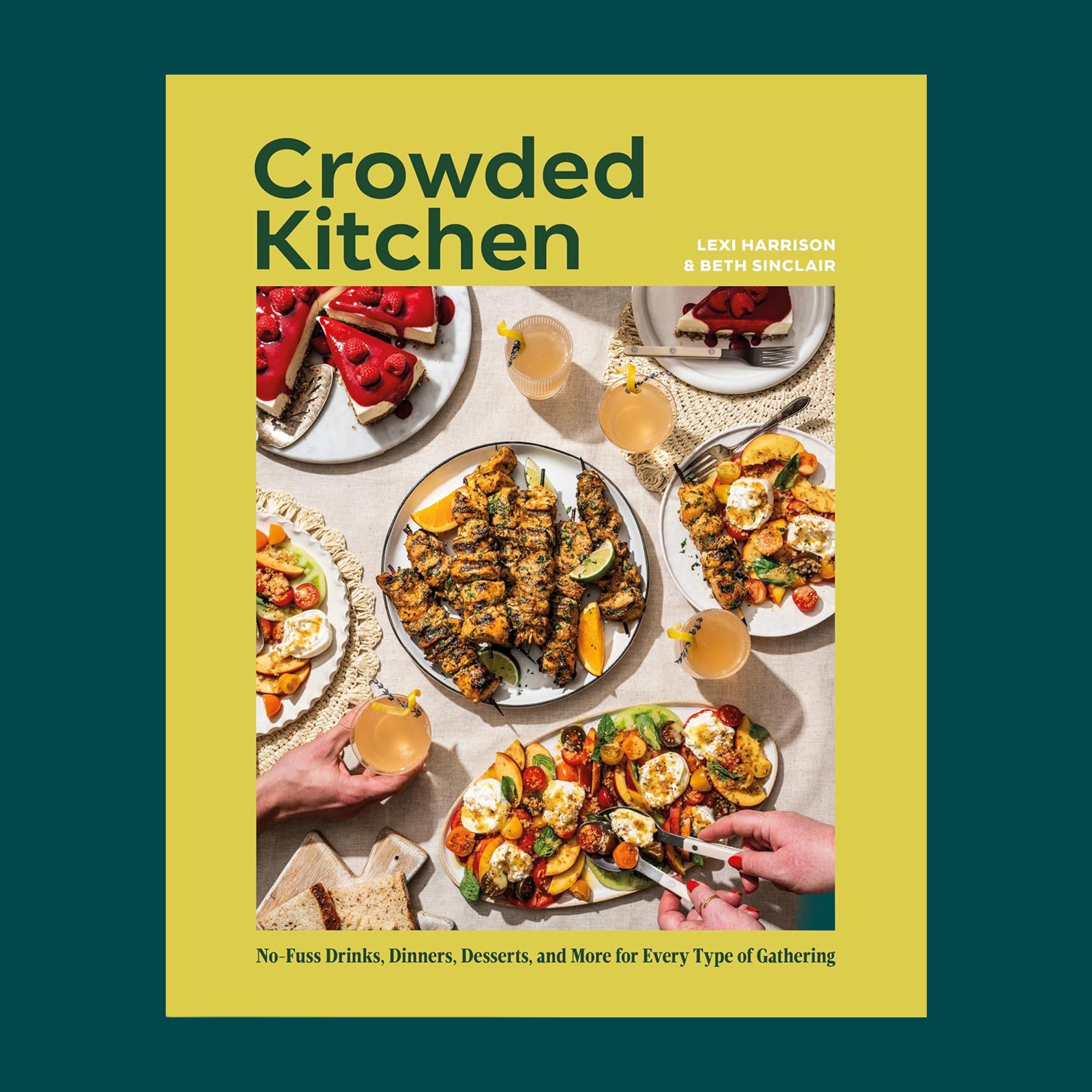 Cover of the cookbook Crowded Kitchen by Lexi Harrison and Beth Sinclair, featuring an overhead table spread with grilled skewers, vegetable dishes, berry cheesecake slices, and drinks shared by several hands.