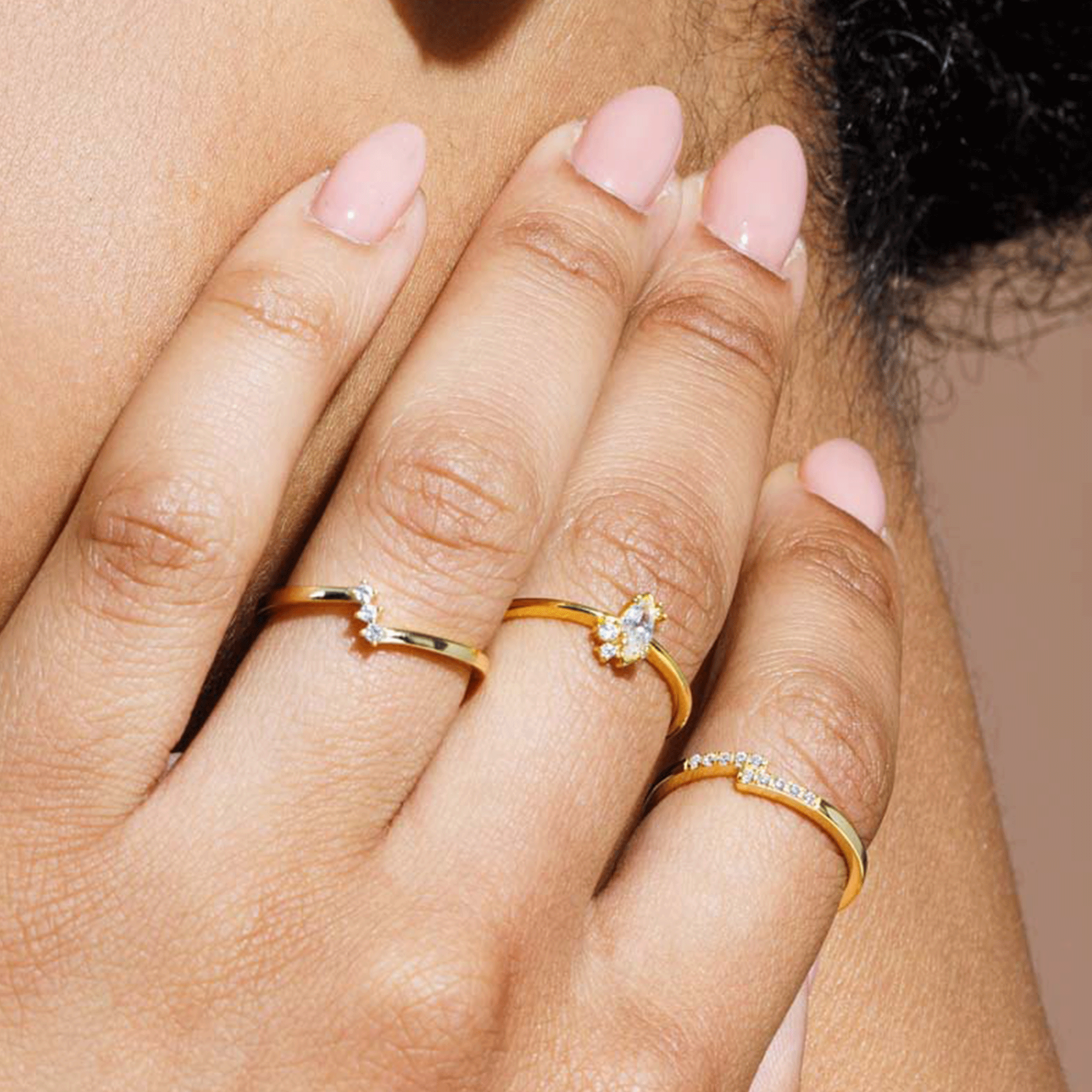 A mode wearing a gold ring with a marquise shaped cubic zirconia with three smaller stones, two towards the bottom and on the top.