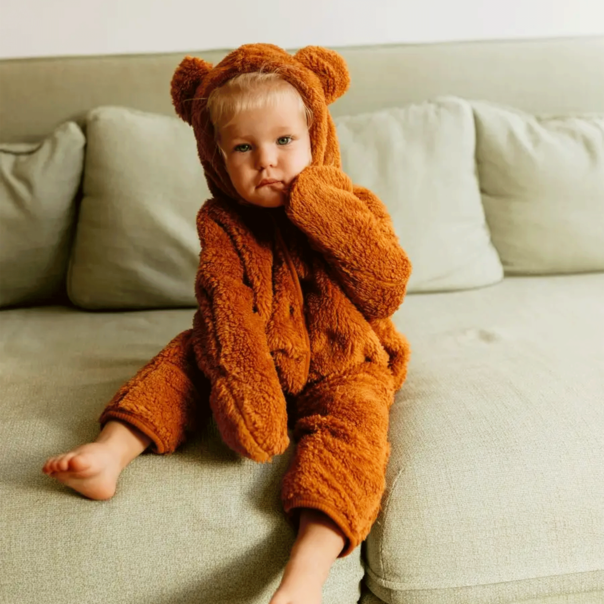 A child wearing a brown fuzzy onesie with a bear shaped ear hoods. 