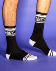 A pair of black and white crew socks that are ribbed with text across the top that reads, "Daddy". 