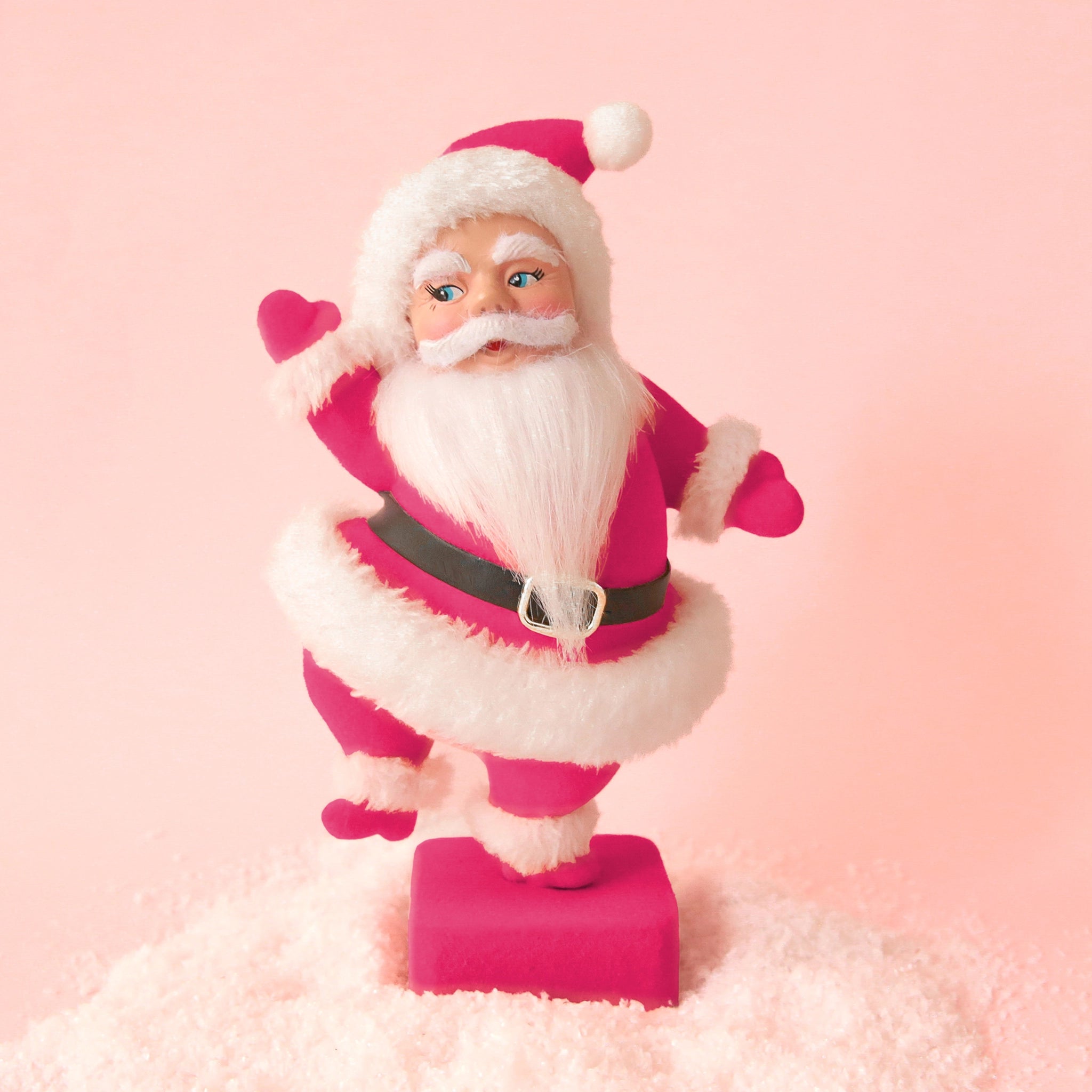 On a peach background is a hot pink flocked Santa shaped figurine holding a dancing pose. 