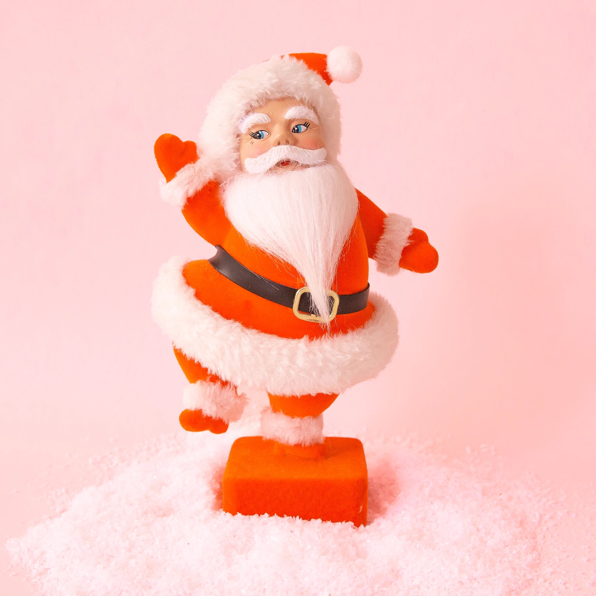 On a peachy background is a red flocked dancing Santa figurine. 