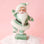 On a pink background is a Santa figurine wearing a mint colored suit with the fluffy details. 