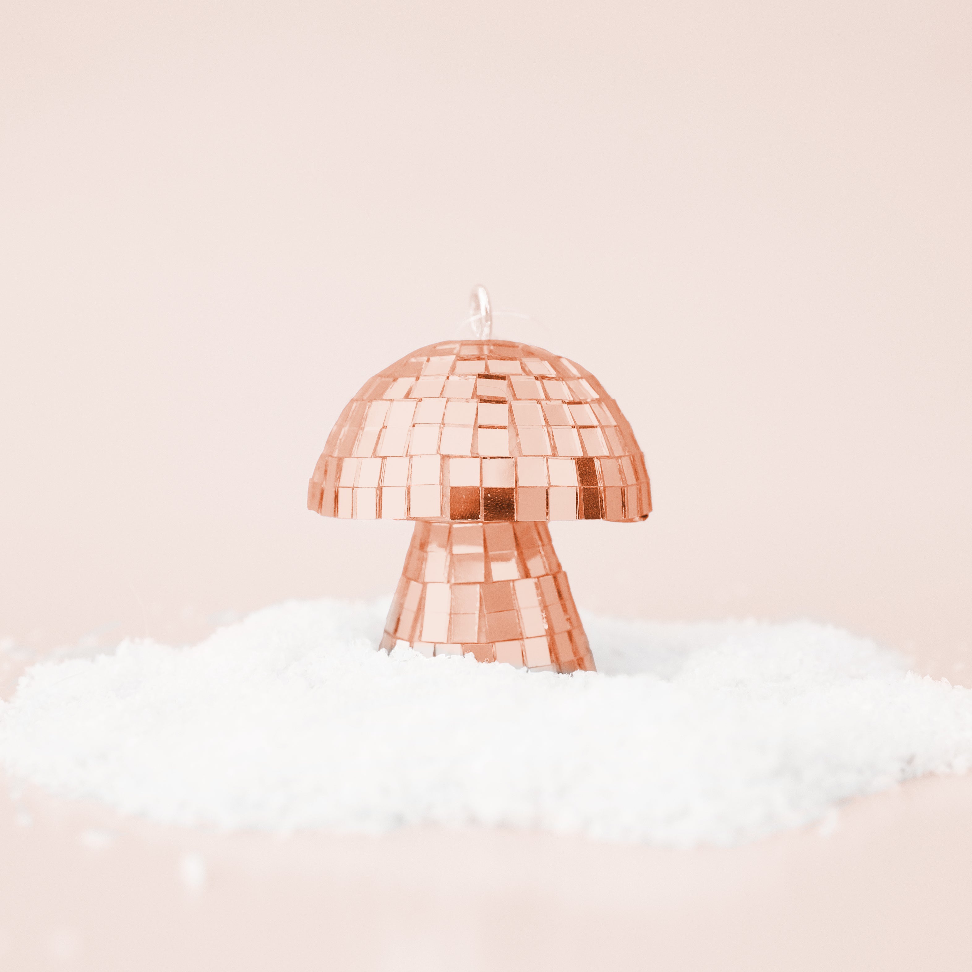 On a neutral snowy background is a rose gold disco mushroom shaped ornament
