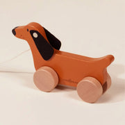 A wooden dog shaped pull toy with wooden wheels. 
