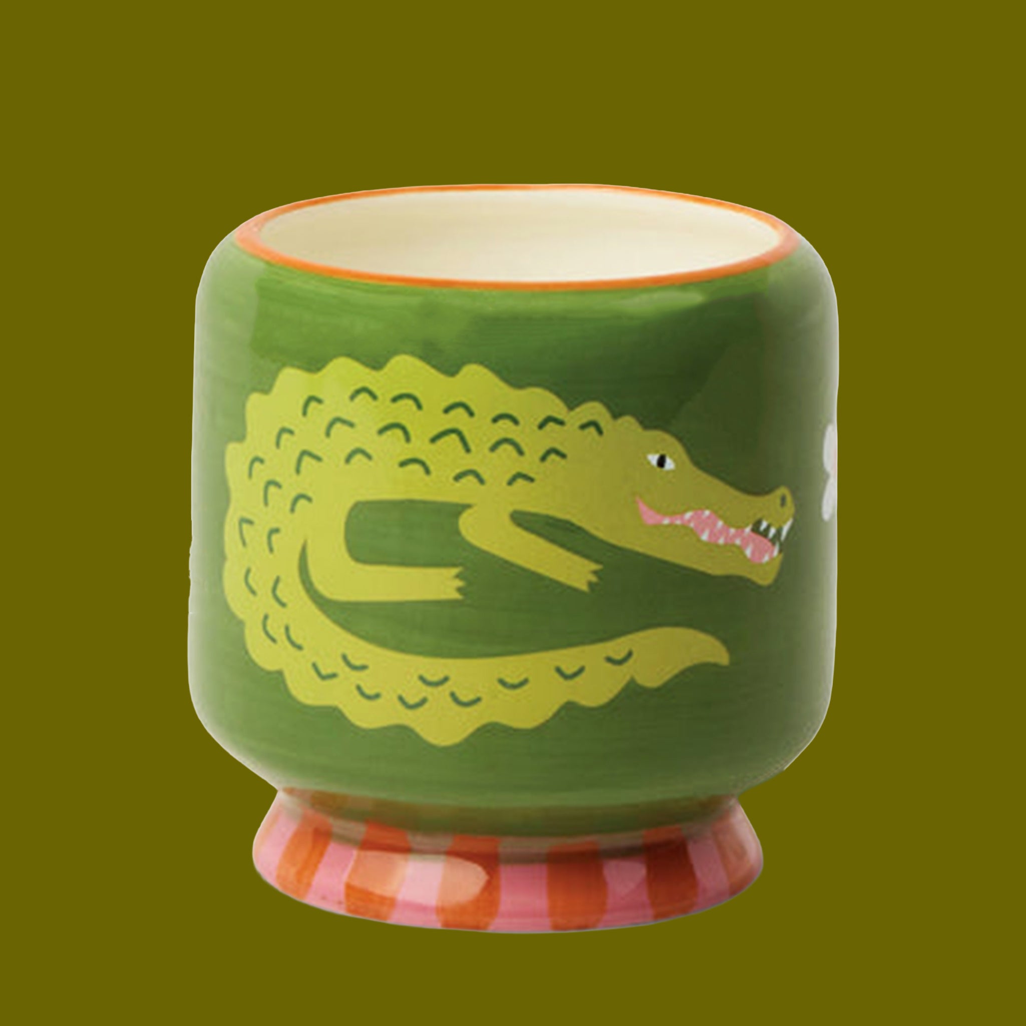 A green ceramic candle with a crocodile motif and red and pink stripes on a green background.