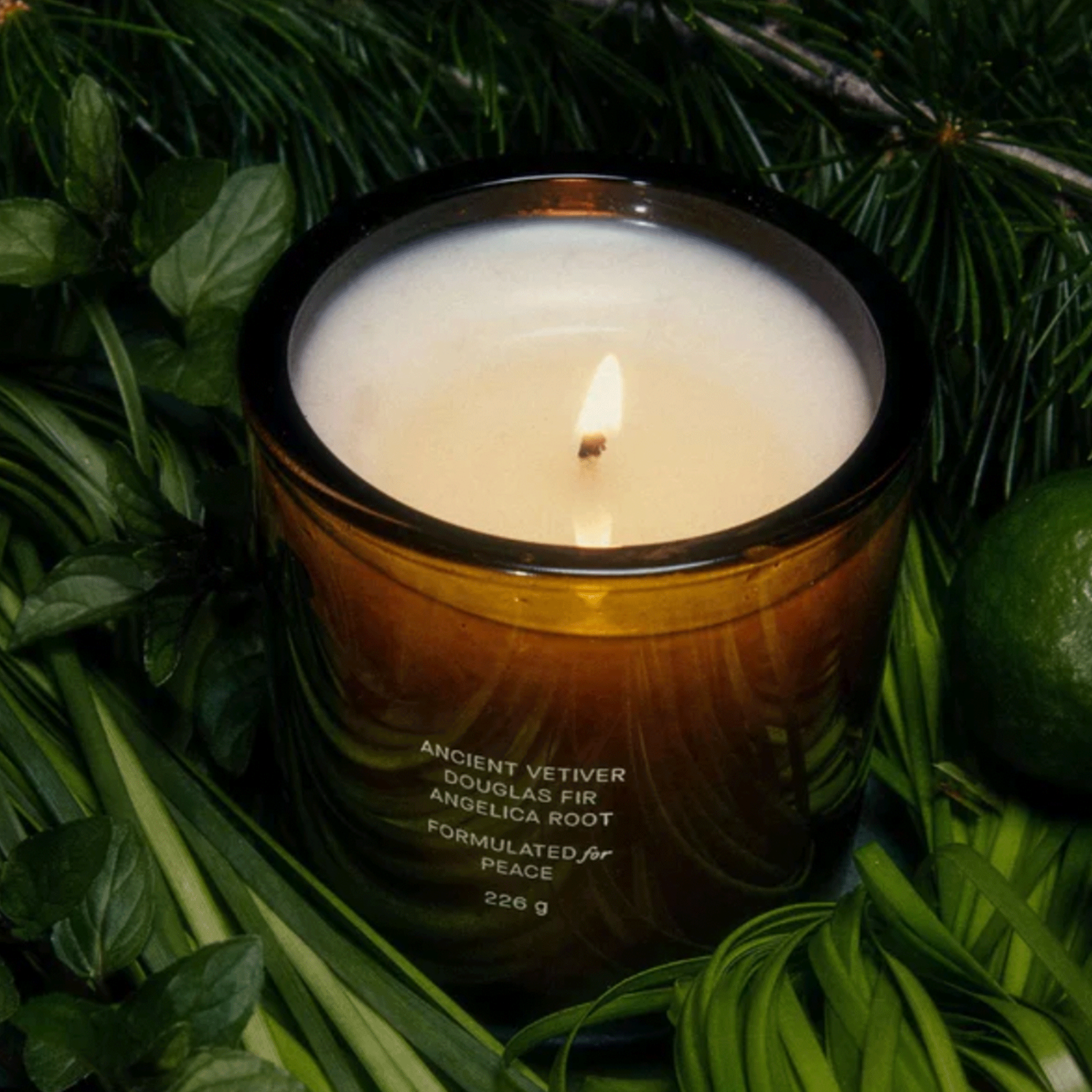 A green glass candle surrounded by basil leaves, fir stems and greenery. 