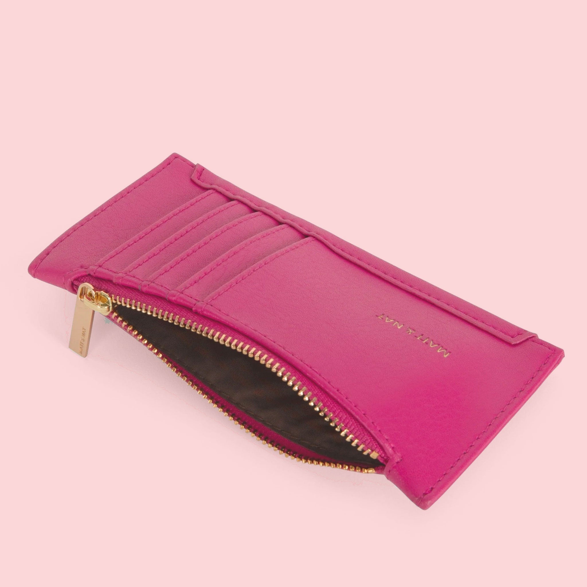On a pink background is a hot pink wallet with card slots on the outside and a zipper.