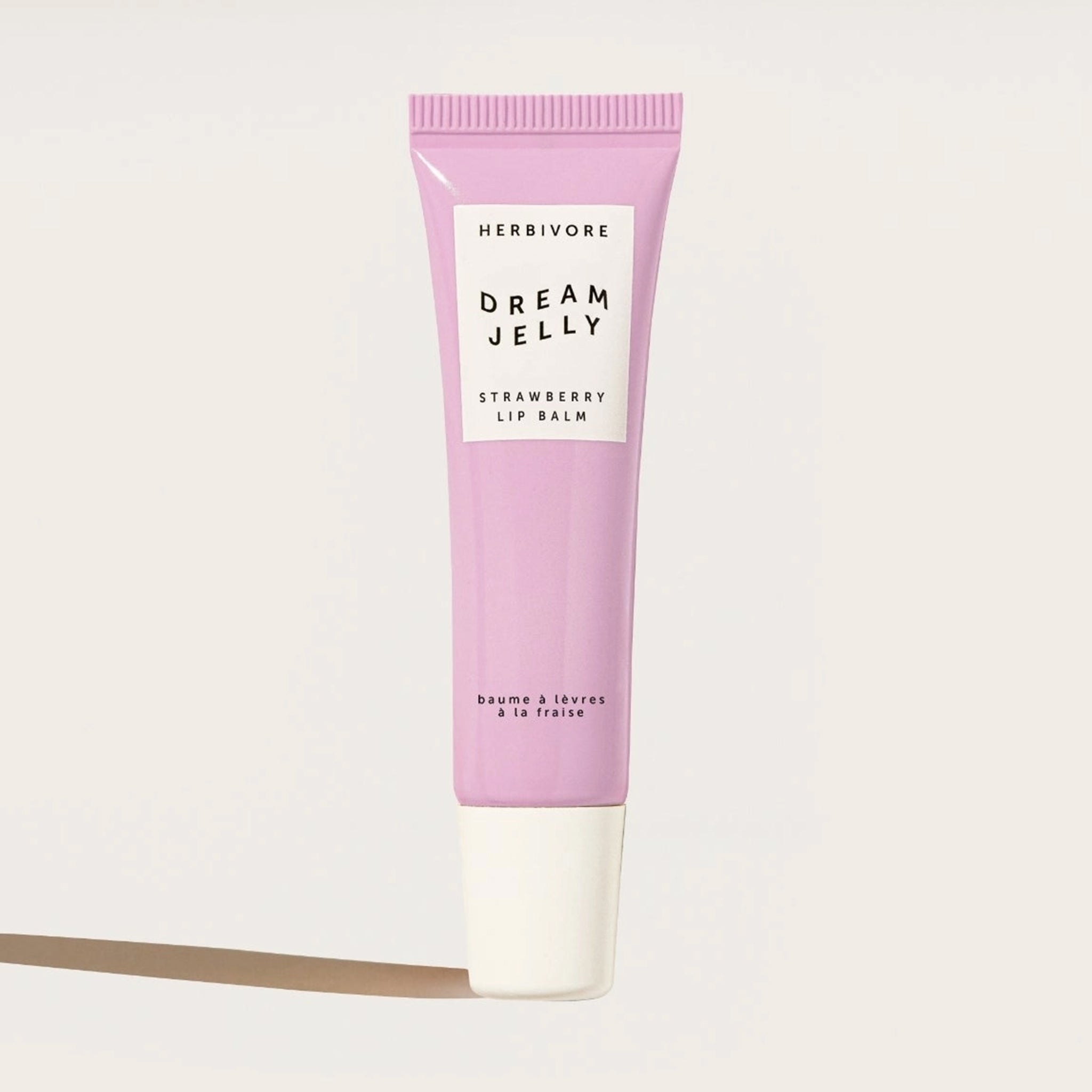 A pink tube of lip balm that reads, "Herbivore Dream Jelly Strawberry Lip Balm". 