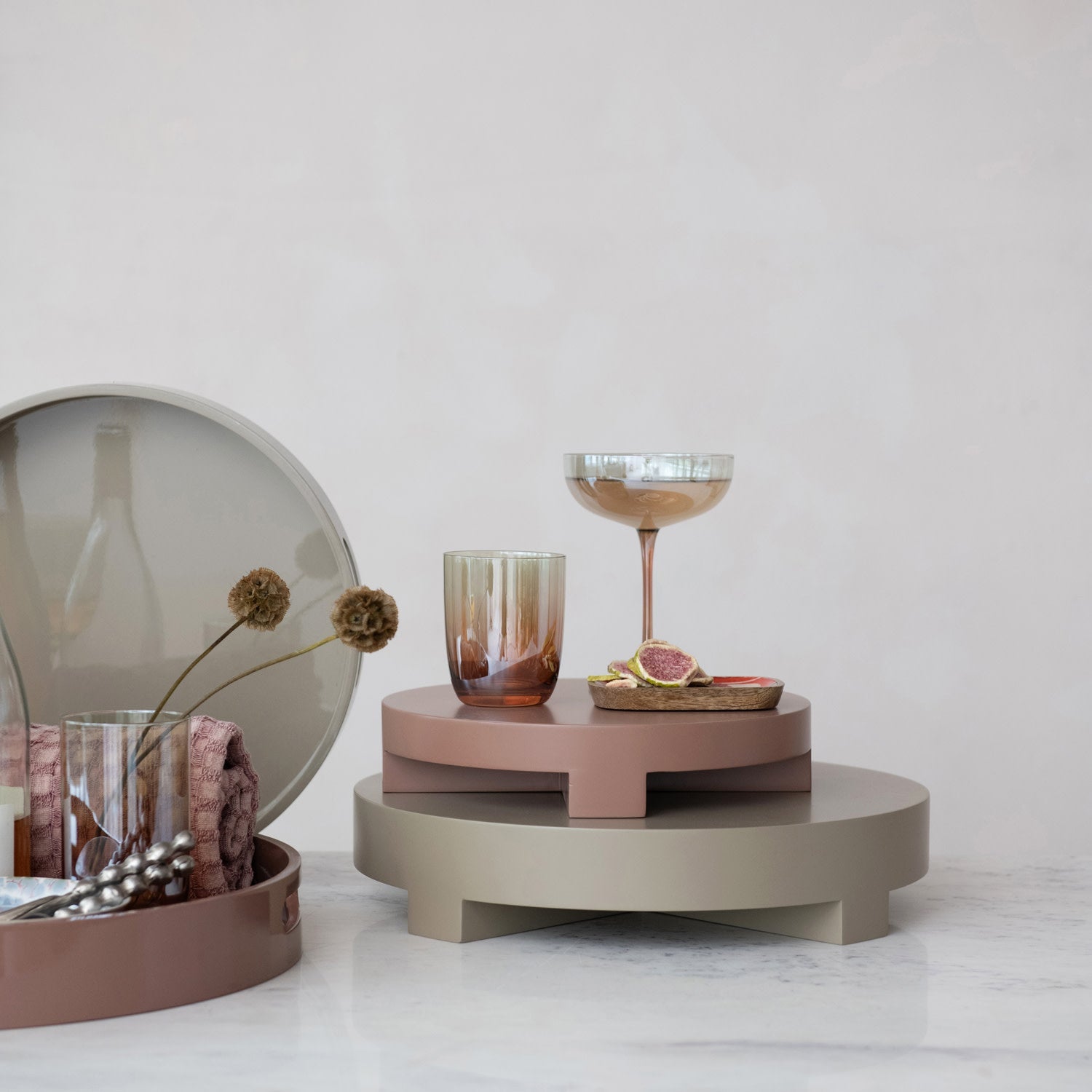 Iridescent drinking glass with amber base displayed beside a coupe glass on stacked serving trays.