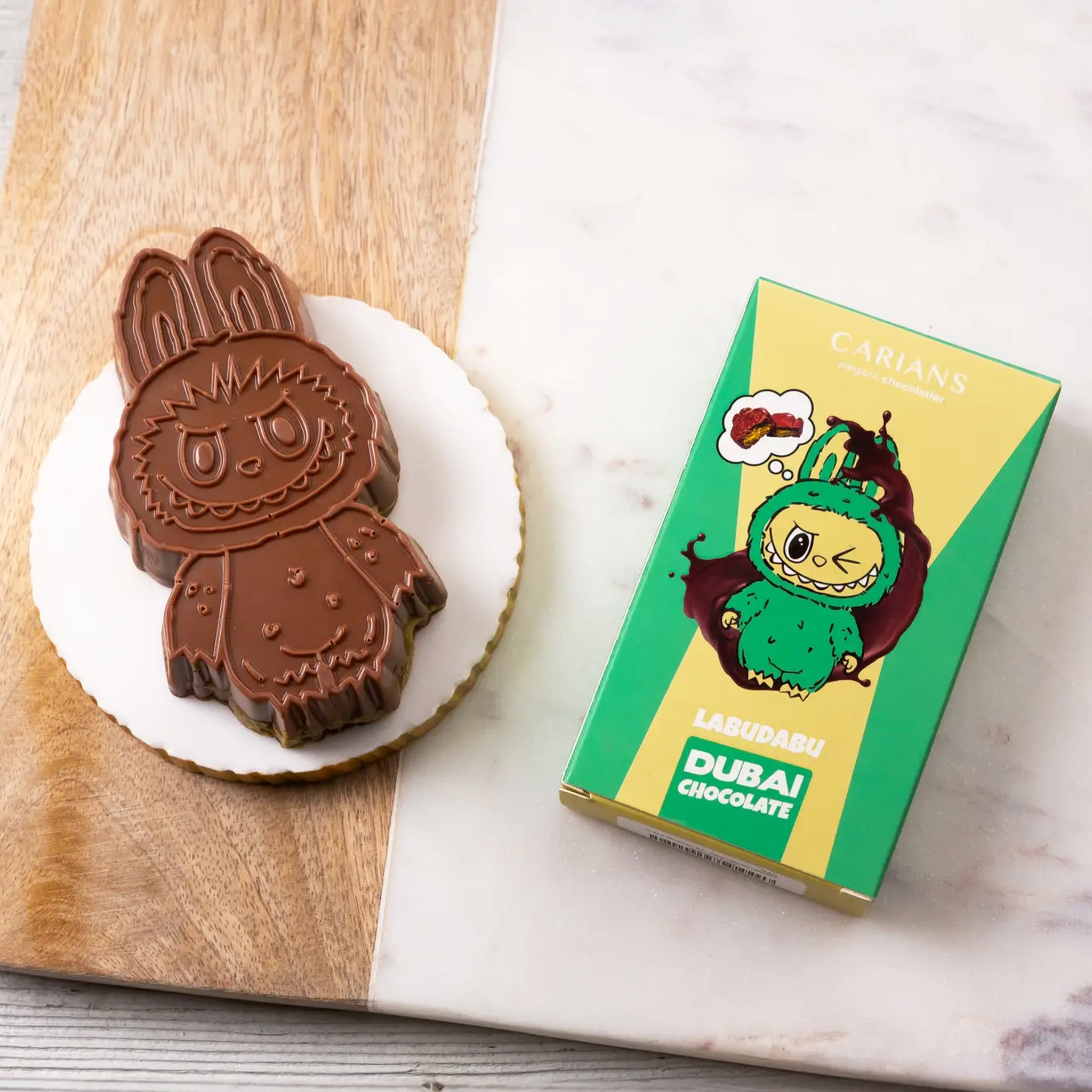 A green and yellow box filled with a Labubu shaped chocolate bar. "Carian's Labudabu Dubai Chocolate". 