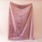 On a tan background is a dusty rose faux fur throw blanket.