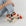 On a white background is a model wearing cream colored socks with a bright red cherries design on it along with "Baggu" on the bottom of the foot. 