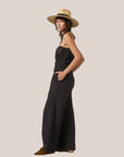 A black jumpsuit with a smocked bust / midsection area and tie spaghetti shoulder straps.