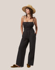 A black jumpsuit with a smocked bust / midsection area and tie spaghetti shoulder straps.