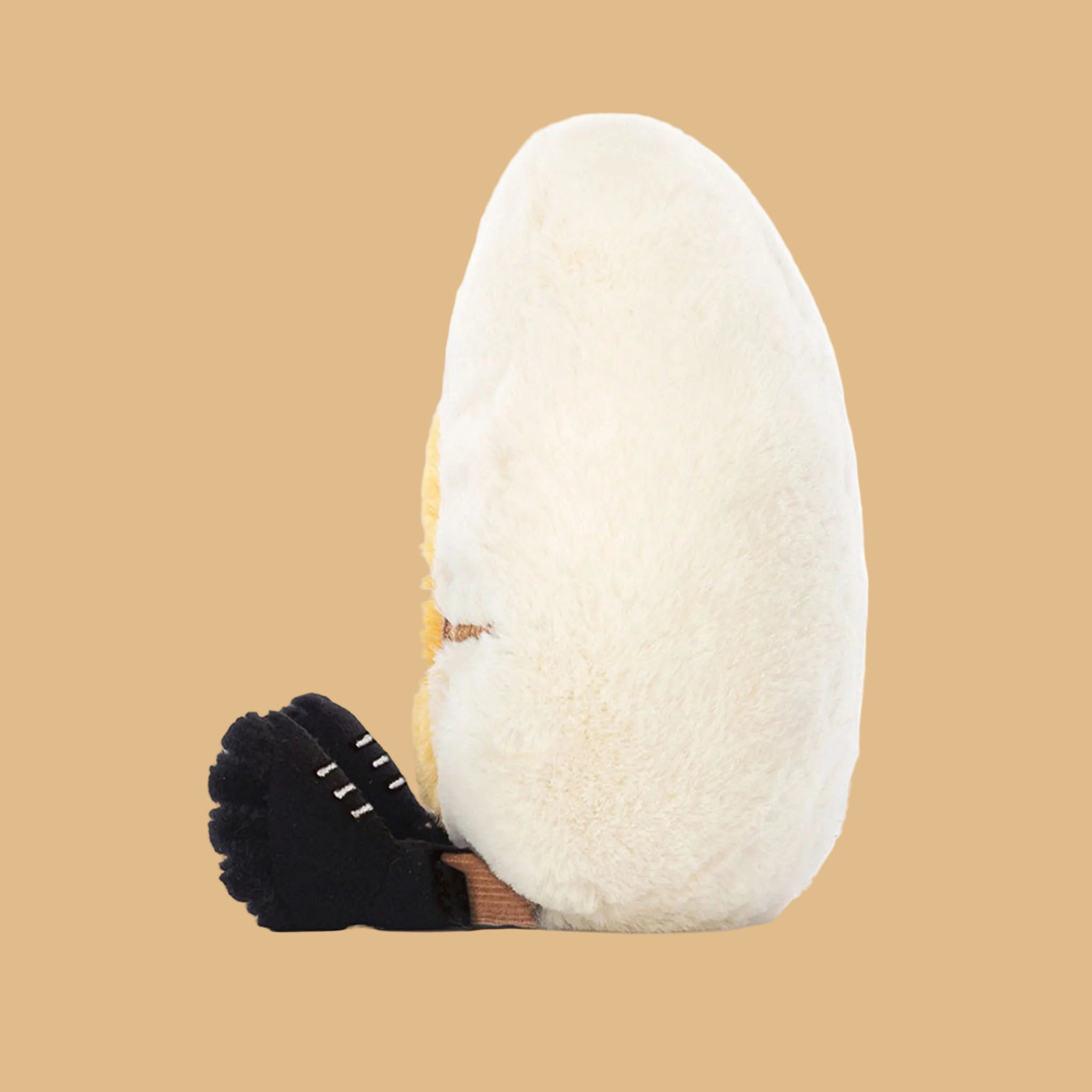 On a white background is a stuffed toy in the shape of a hard boiled egg with sunglasses on and small legs and feet. 