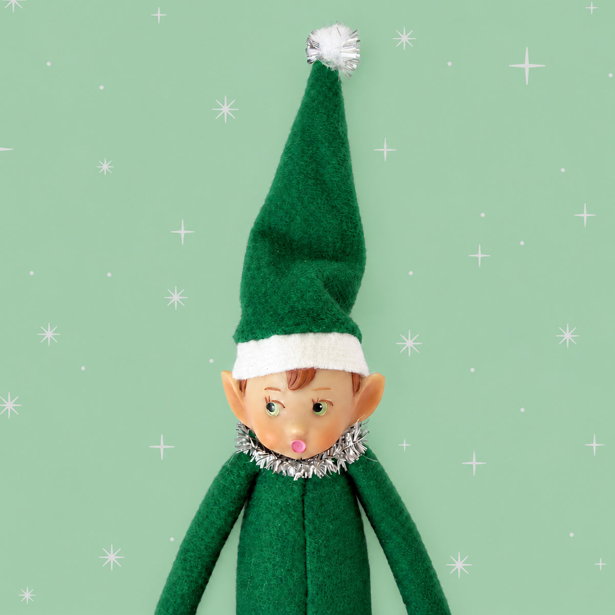 Green elf ornament on a mint green background with white stars. 