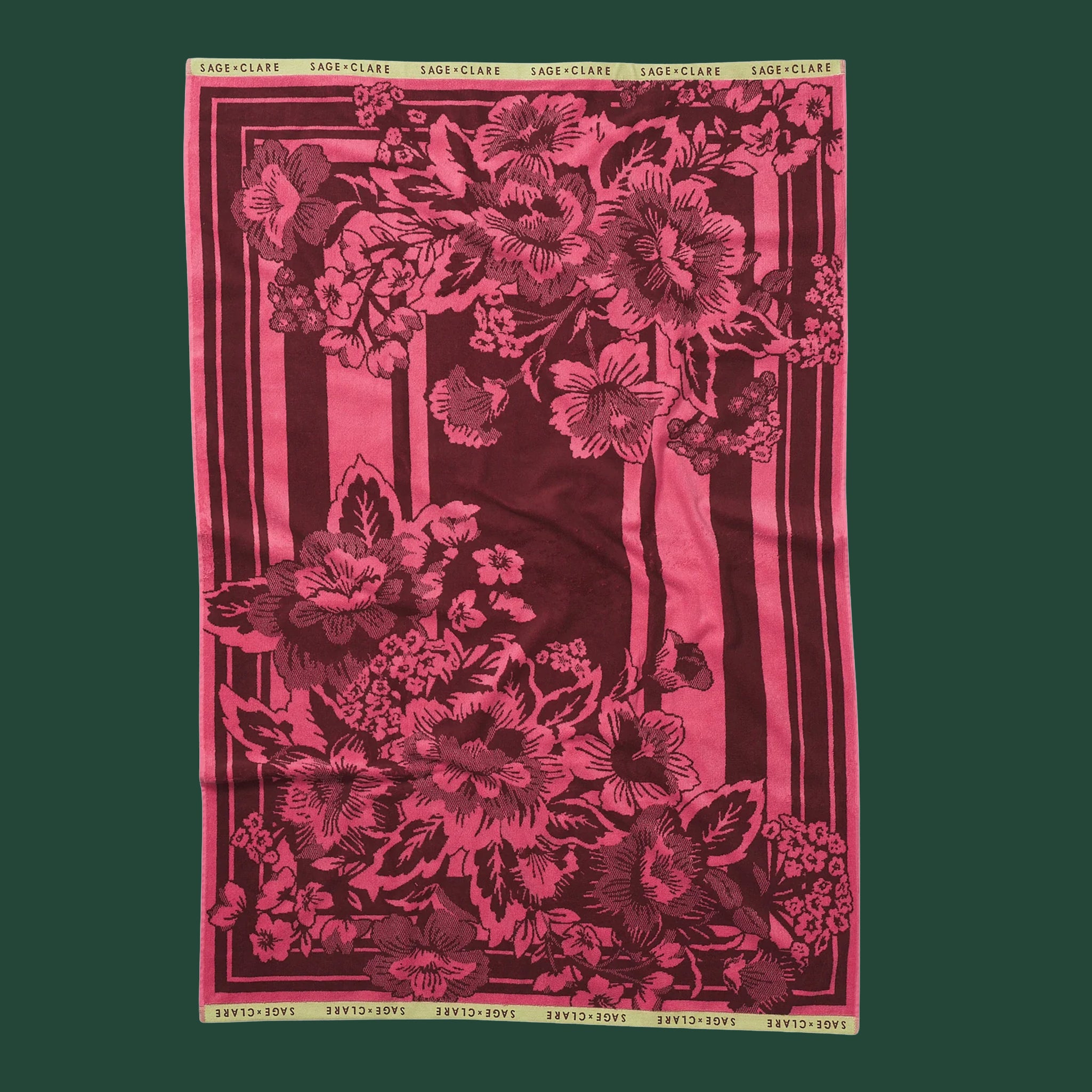 A beautiful pink and maroon bath towel with a floral motif on a ark blue green background.