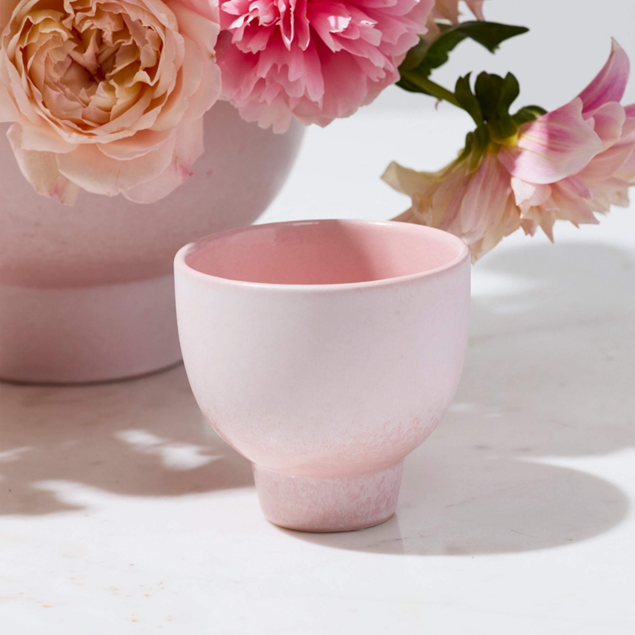 A ceramic pedestal bowls / vase that is pink. 