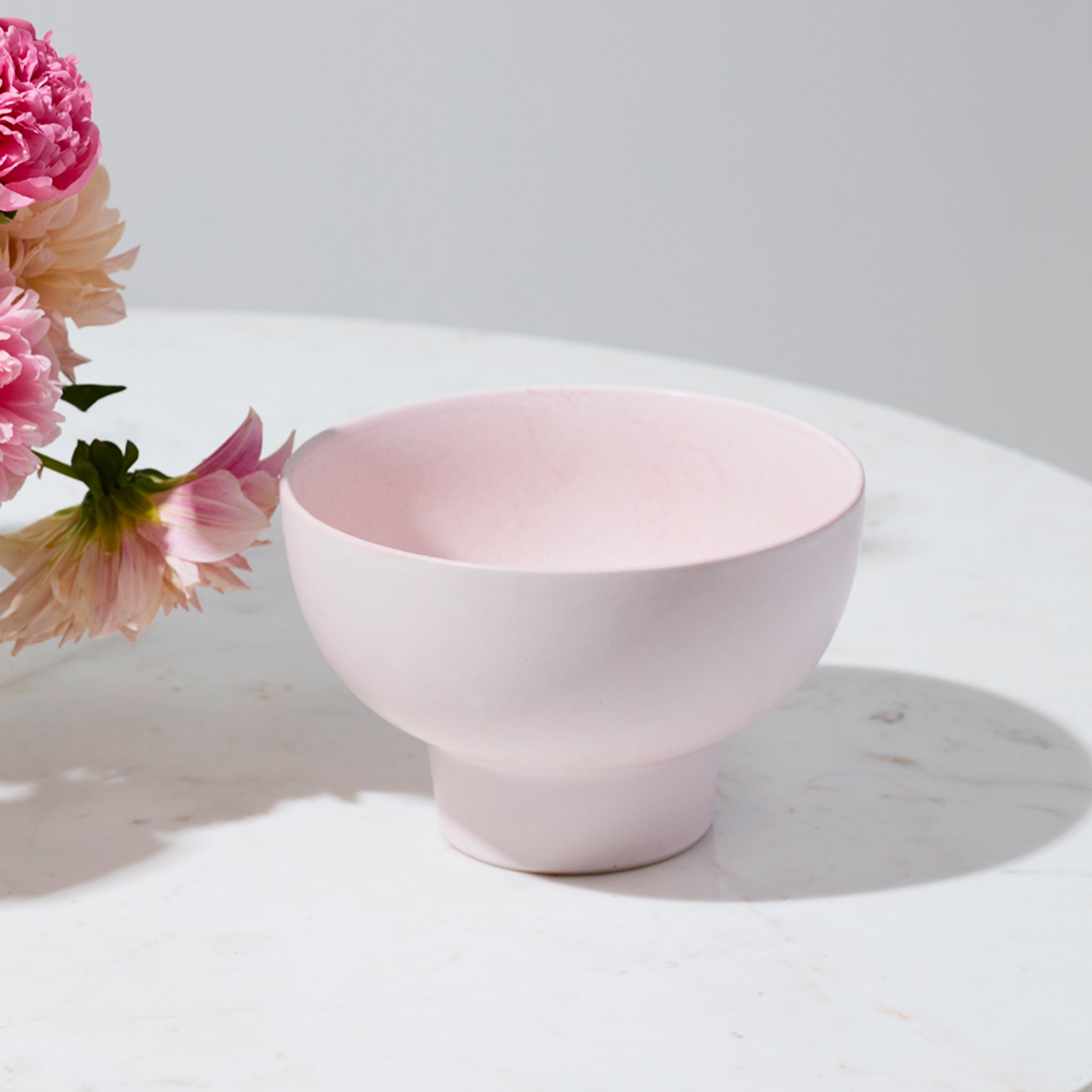 A ceramic pedestal bowls / vase that is pink. 