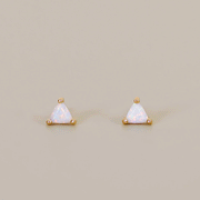 On a tan background is a triangle shaped stud earring with gold plating and a white opal stone center. 