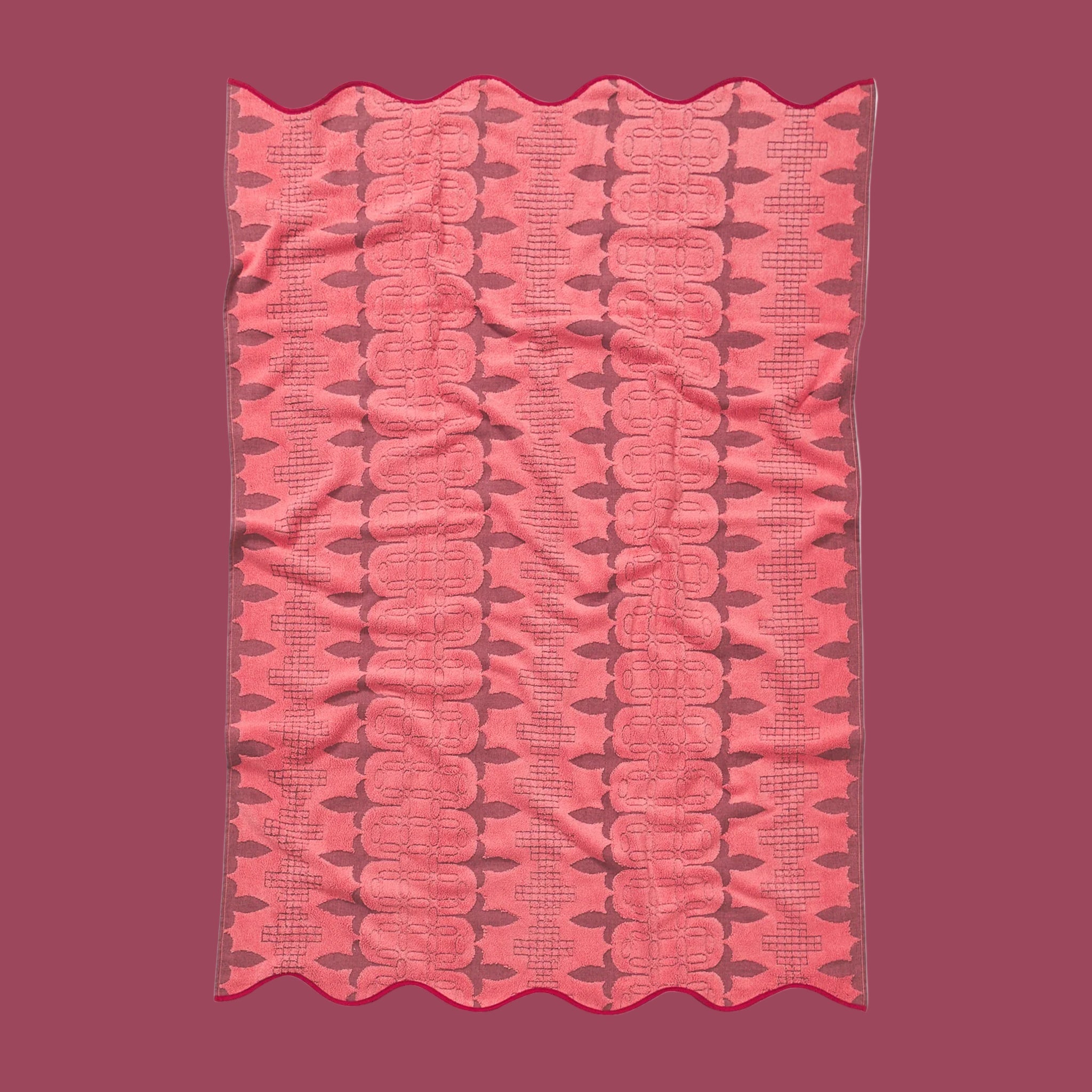 A pink and red piping edge bath towel with a wavy end on both sides. 