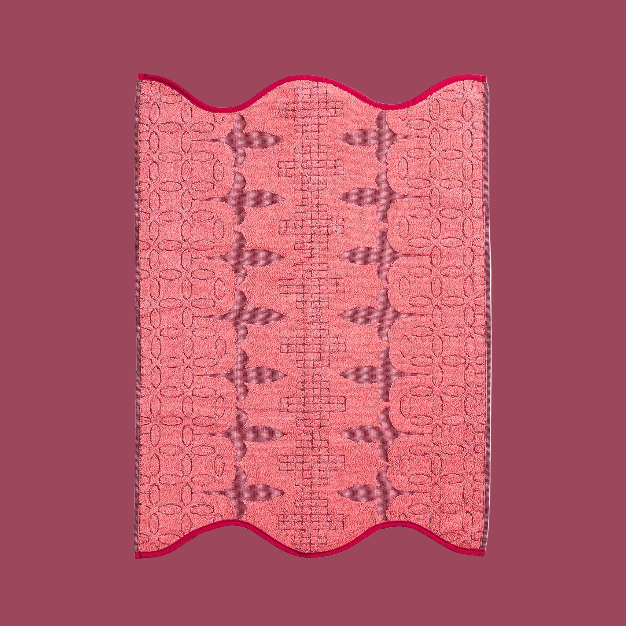 A pink and red piping edge hand towel with a wavy end on both sides. 