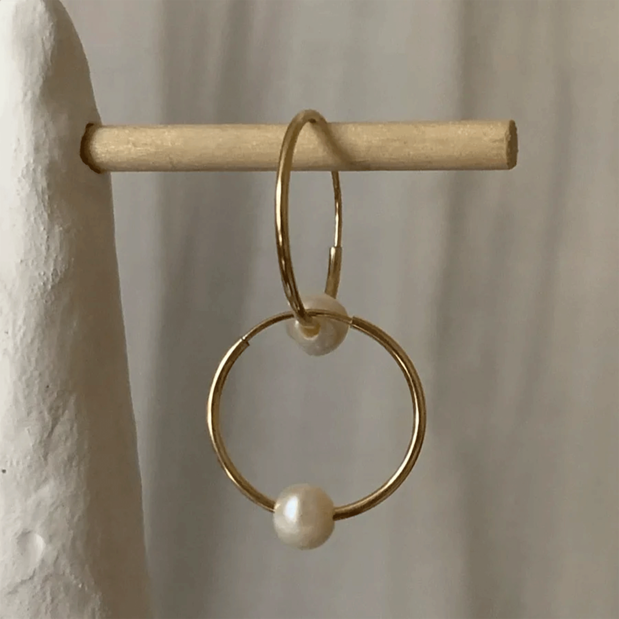 On a tan background is a pair of gold hoop earrings with a pearl on the bottom of each hoop. 