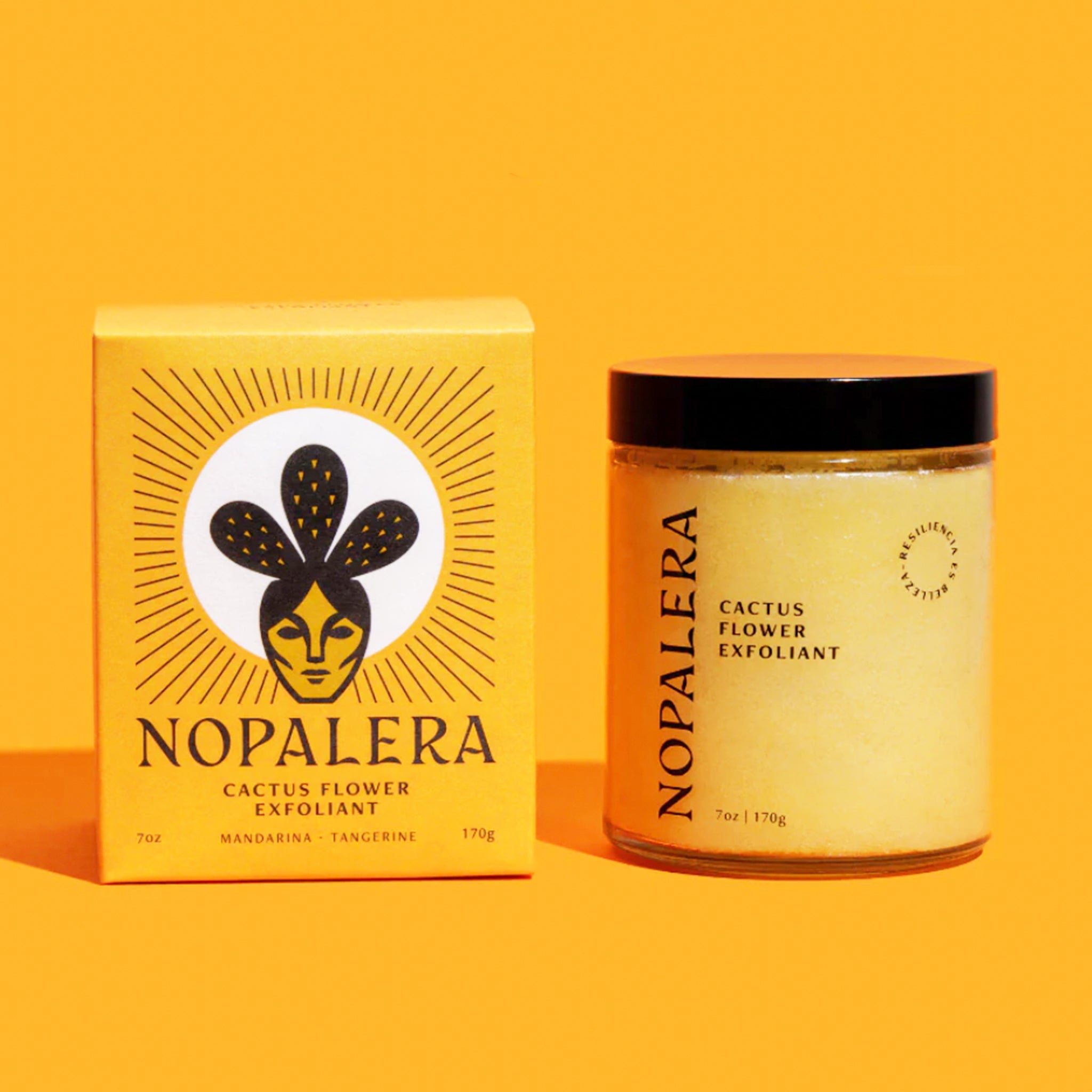 On a bright yellow background is a box with a design of a woman with cactus behind her head along with a jar of exfoliant that reads, "Nopalera Cactus Flower Exfoliant". They are both a similar shade of yellow and have a black screw on lid.