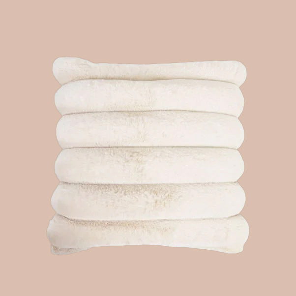 A cream colored faux fur pillow.
