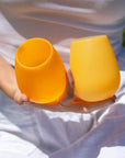 A pair of stemless silicone cups, one light yellow and the other darker.