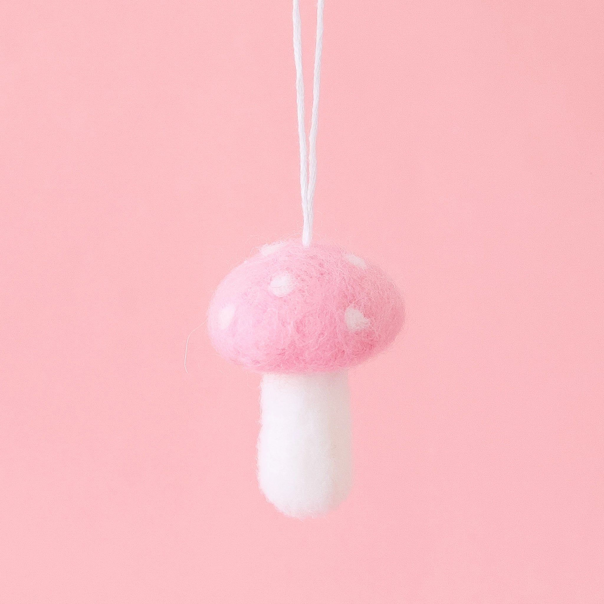 On a pink background is a felt mushroom shaped ornament with white accents. 
