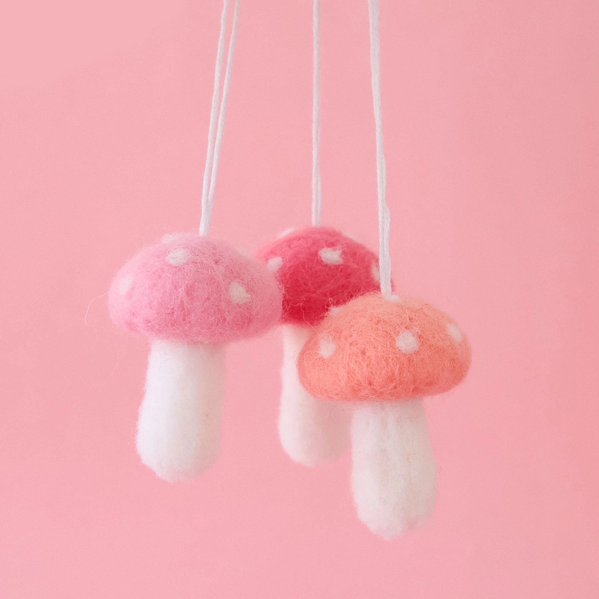 On a pink background is all three available colors of the felt mushroom ornament. There is a dark pink, light pink and peach option.