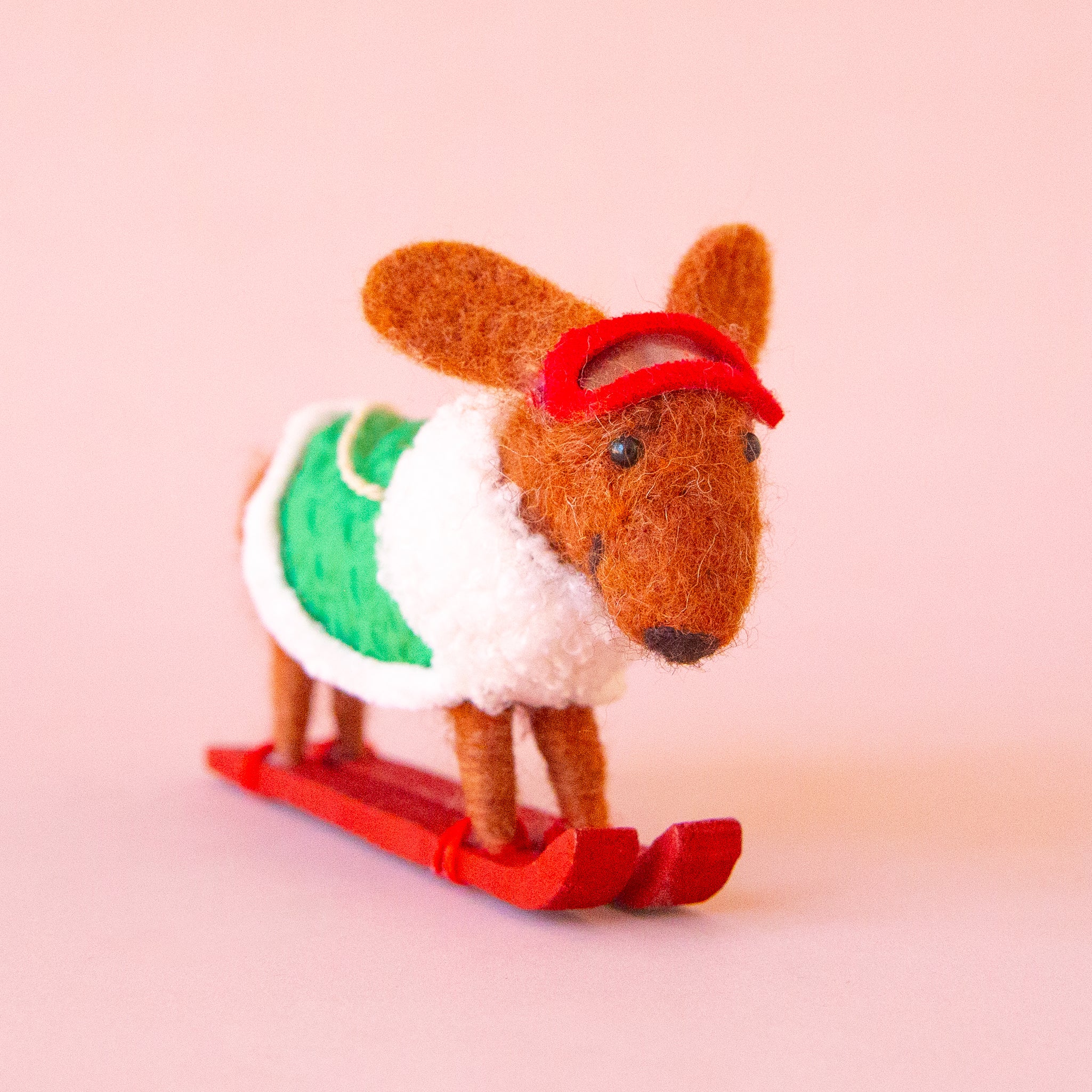 A brown dachshund shaped ornament on skis and wearing a green jacket. 