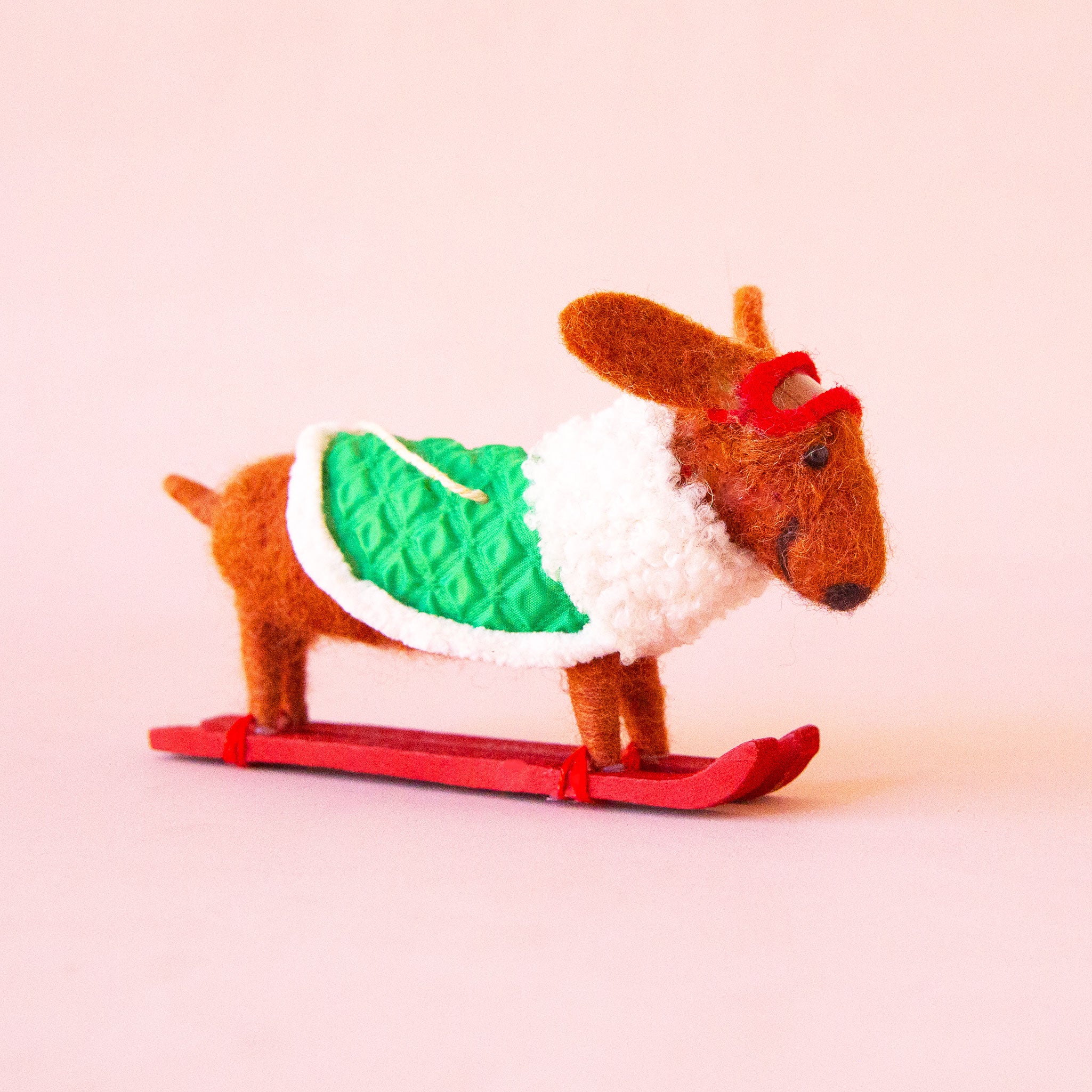 A brown dachshund shaped ornament on skis and wearing a green jacket. 