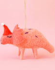 On a pink background is a coral colored felt dinosaur with a red santa hat.