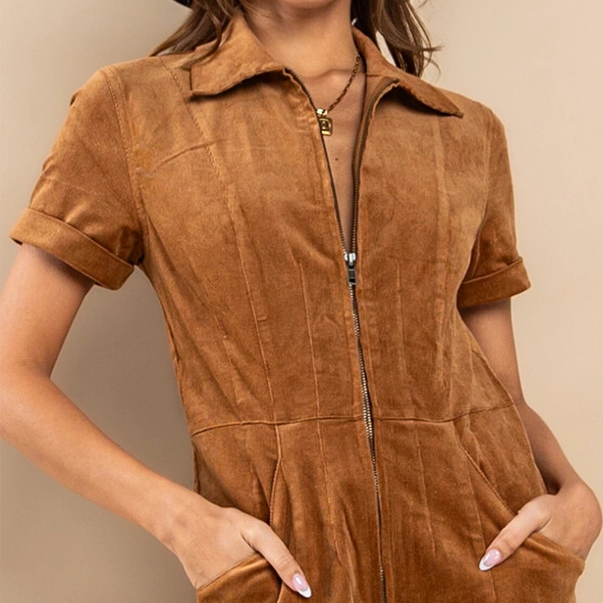 On a tan background is a short sleeved zipper jumpsuit in a camel shade.