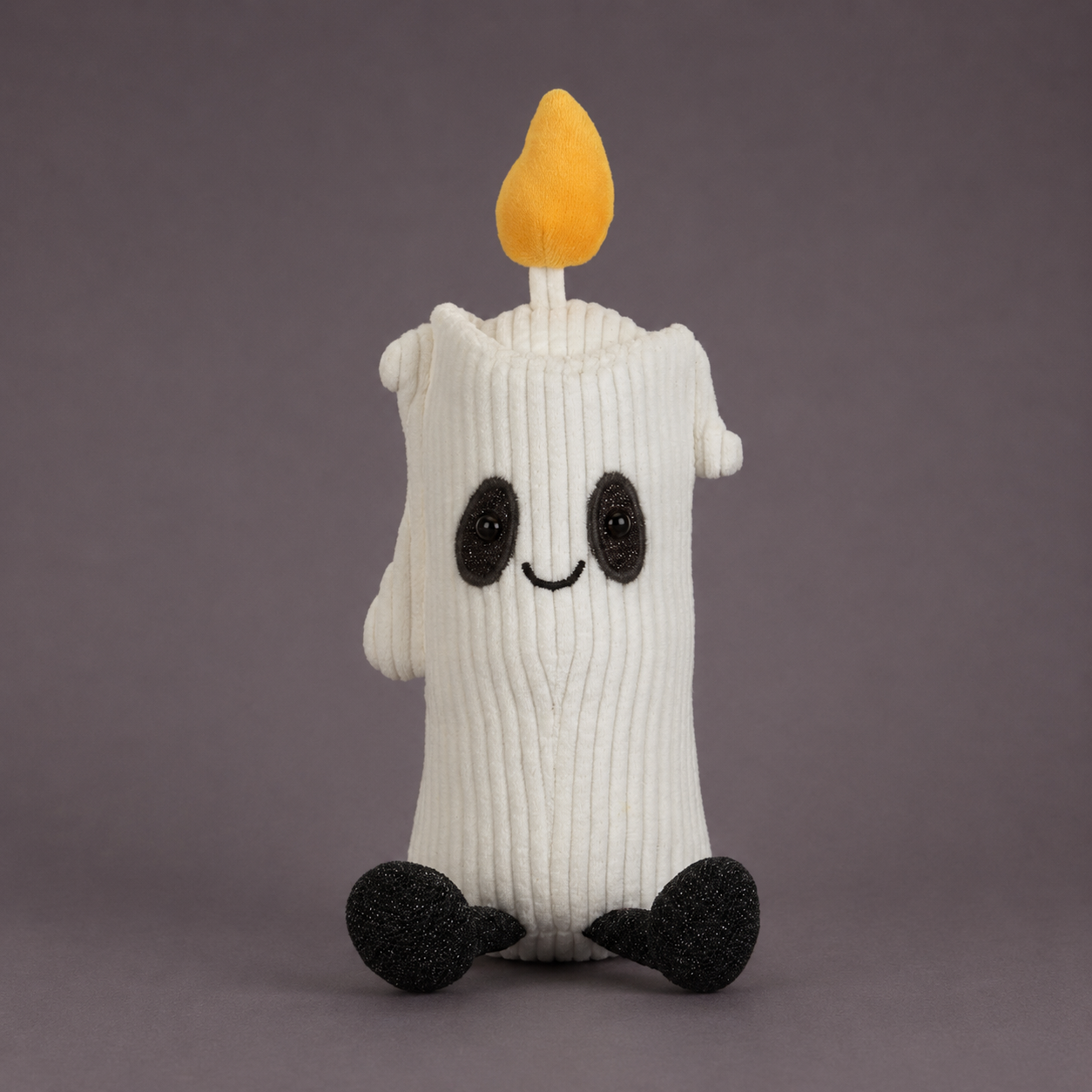 A white ribbed knit candle-shaped plush toy with a yellow flame on top, black embroidered eyes and mouth, and black feet, photographed against a plain dark gray background.