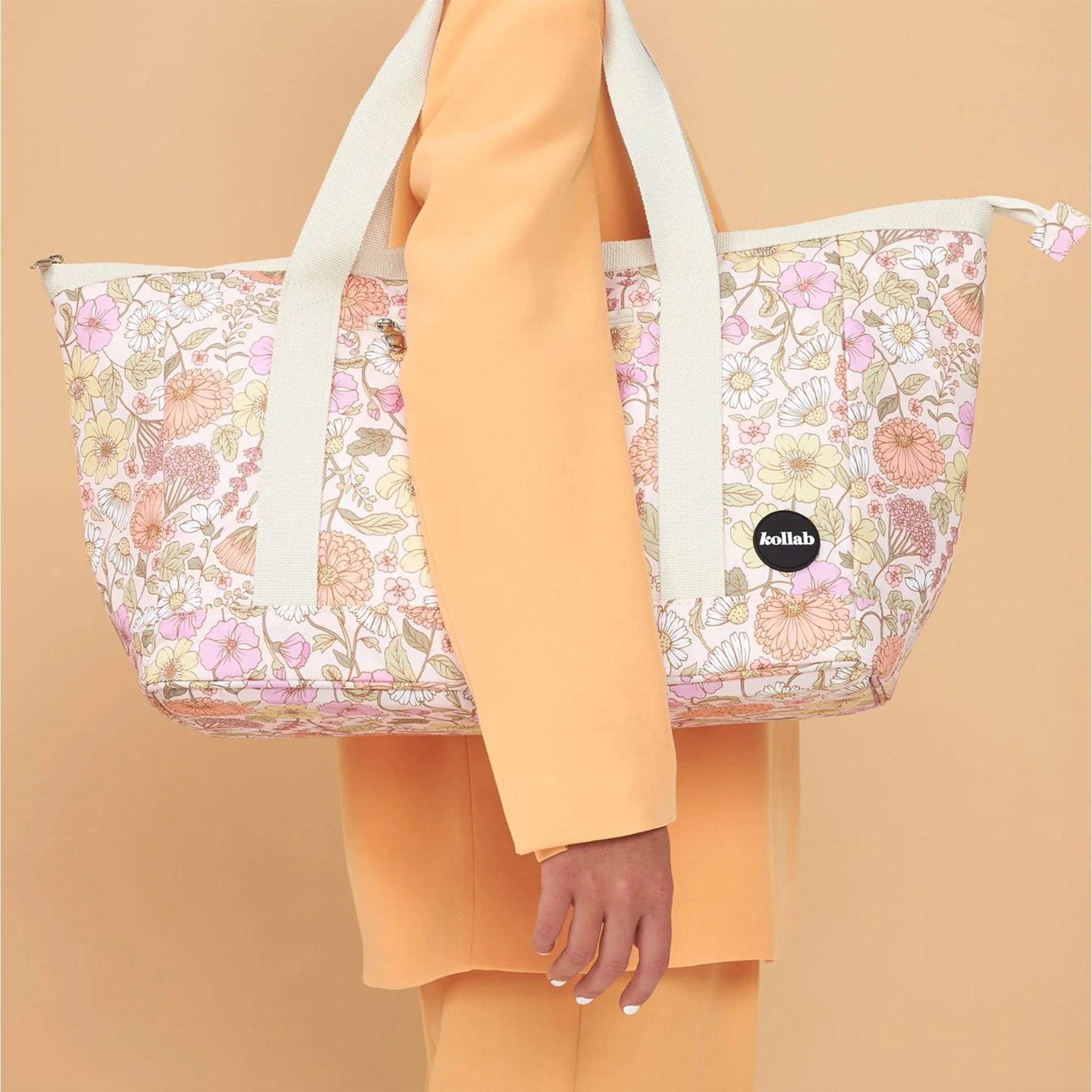 On an orange background is a floral printed tote bag with an ivory strap. 