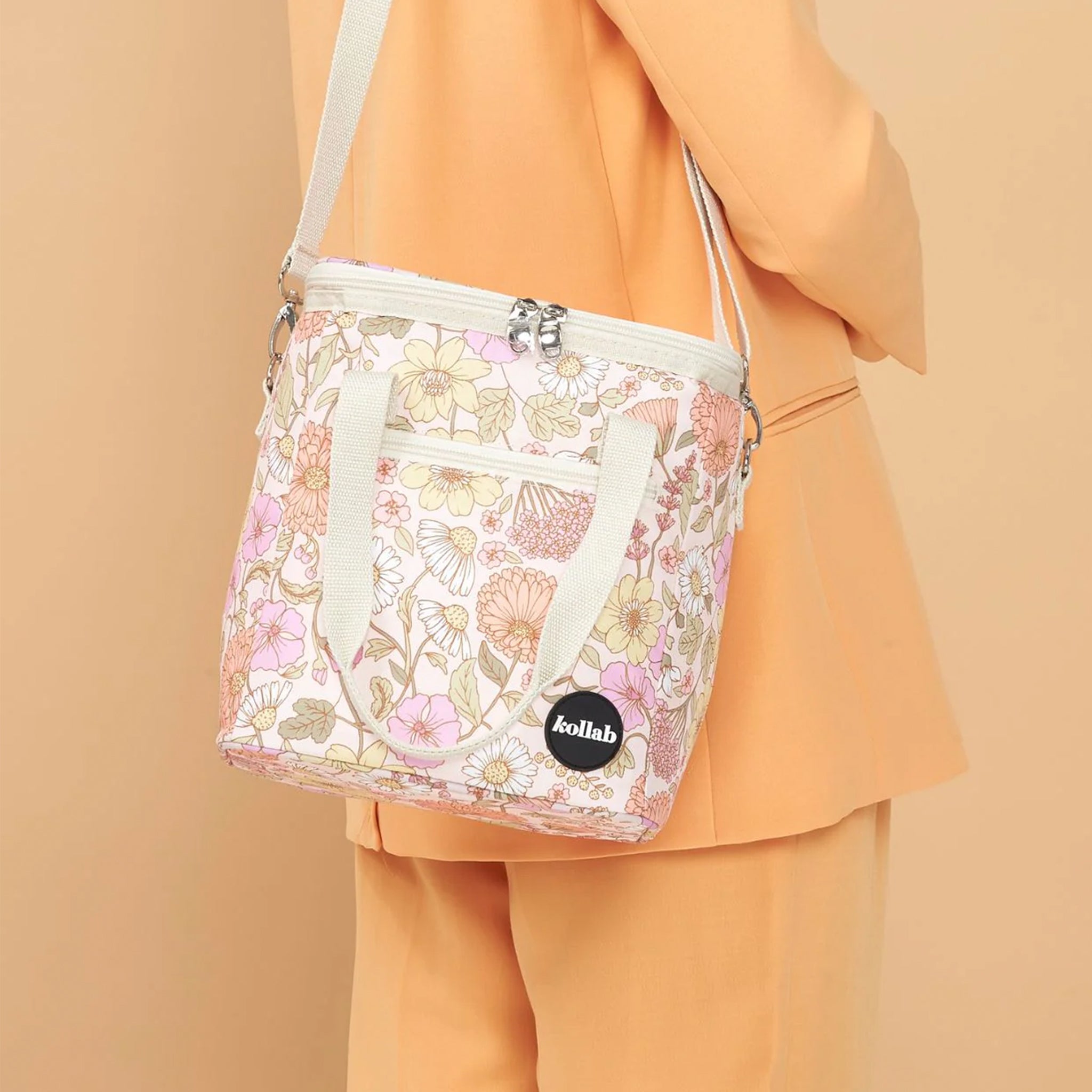 A pink and yellow muted floral printed cooler bag with a strap. 