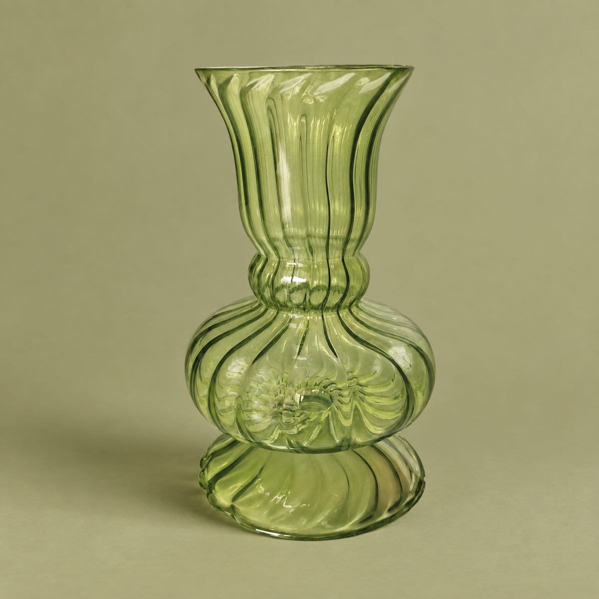 A  light green ribbed glass vase with a flared rim, a bulbous base, and a small pedestal foot, set against a solid beige background.
