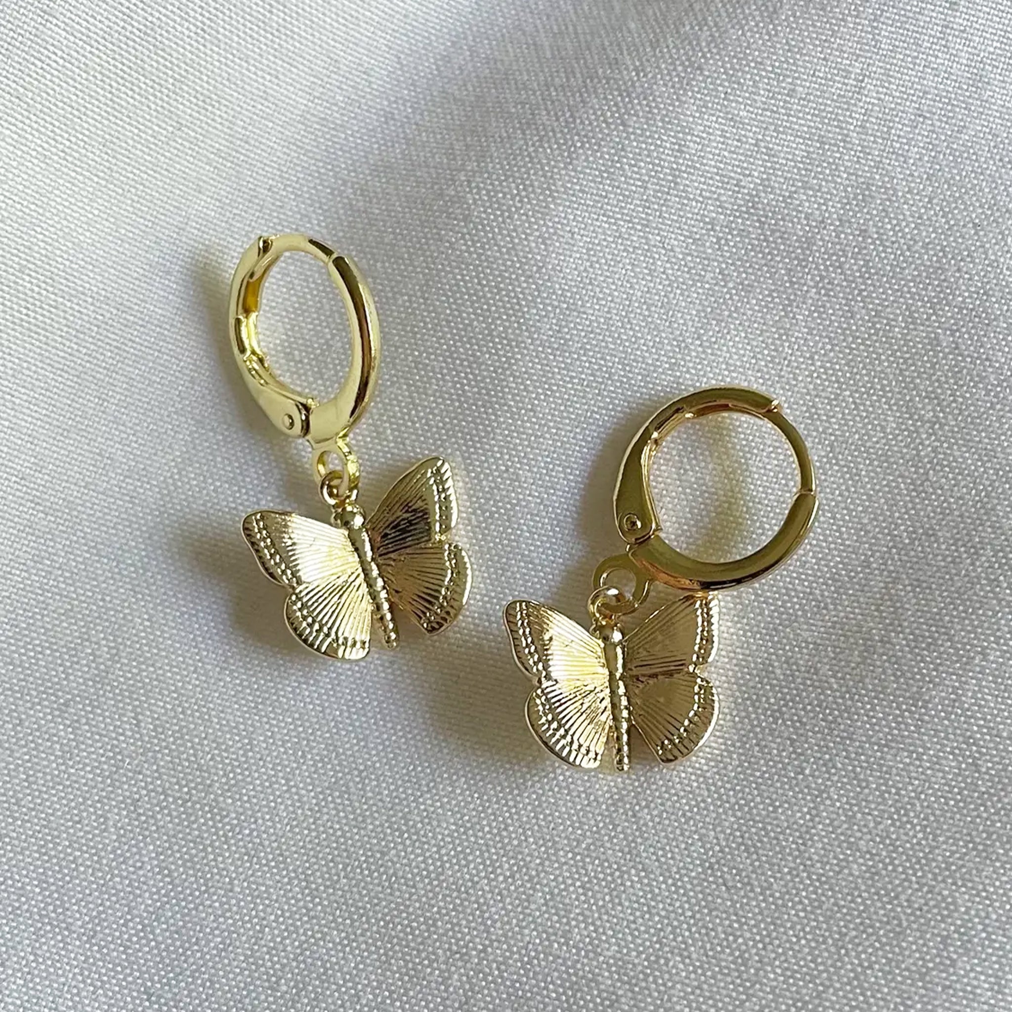A pair of gold huggie earrings with butterfly charms. 