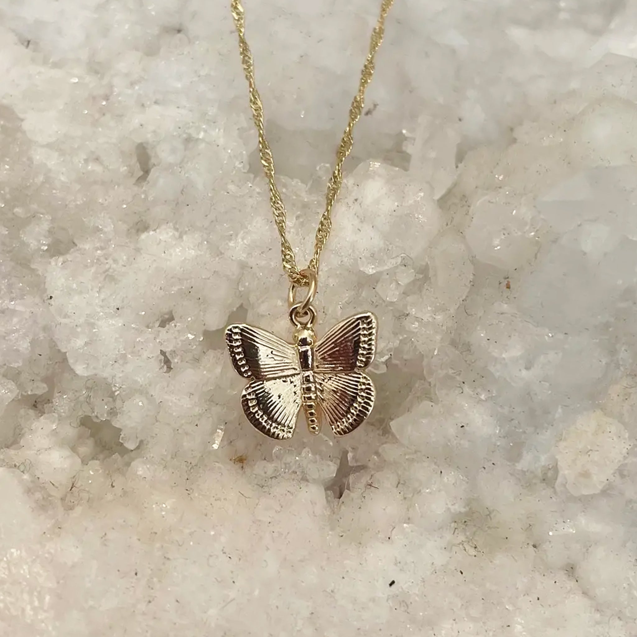A gold chain necklace with a gold butterfly pendant. 