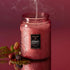 A red decorative glass jar with a black label in the center that reads, "Foraged Wildberry". 