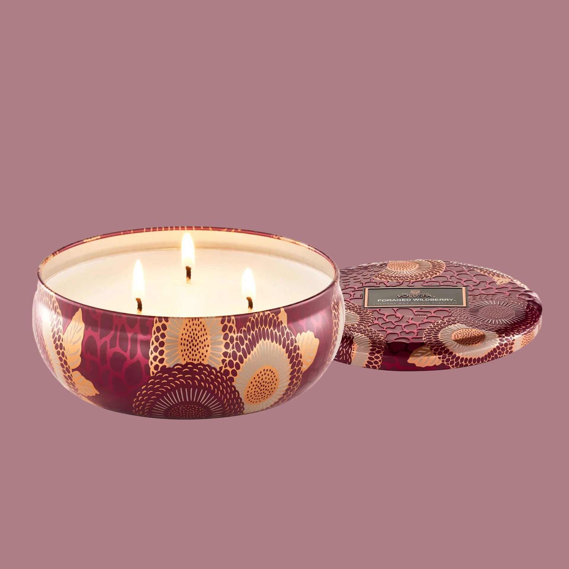 A red and tan floral print metal tin with a three wick candle inside. 
