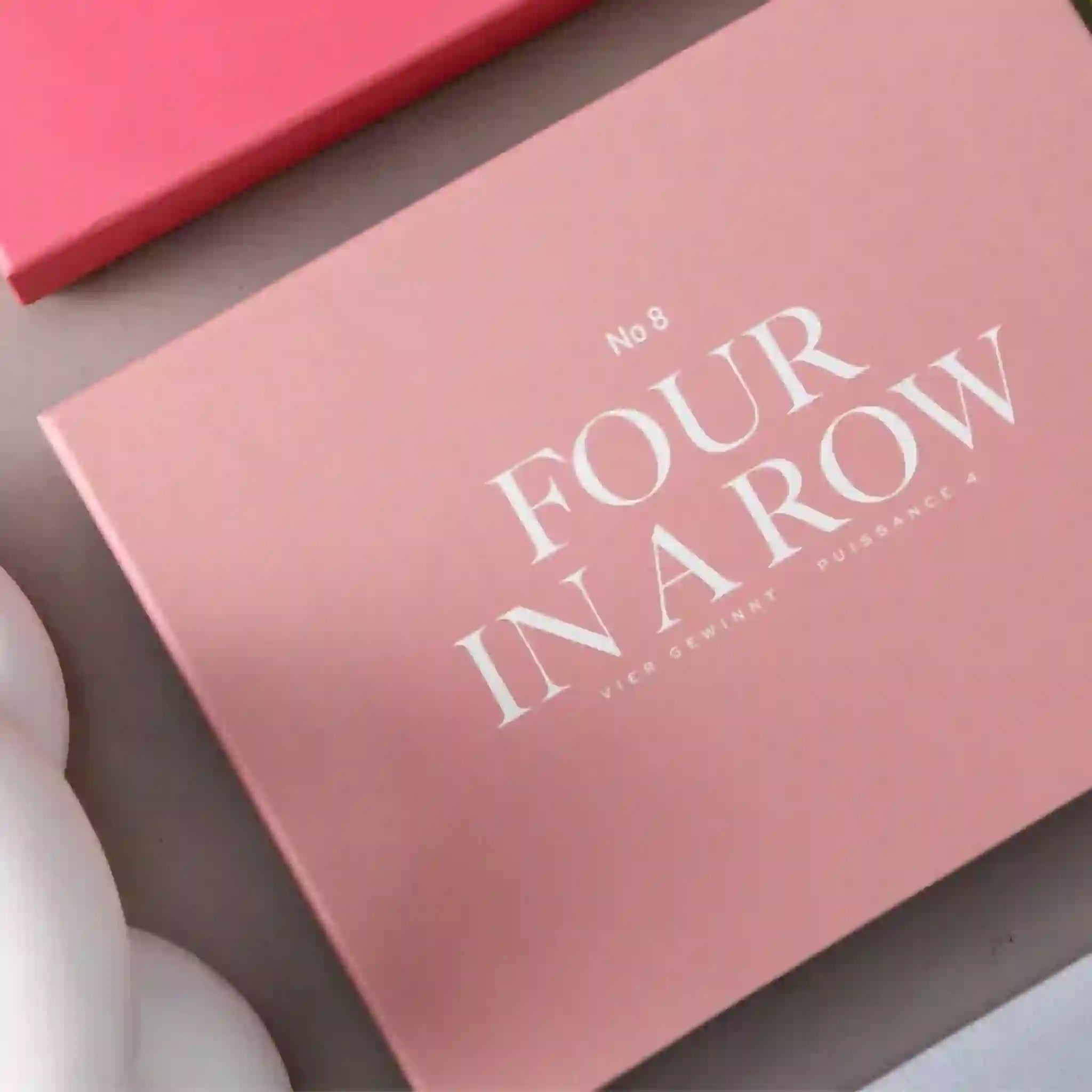 A pink box filled with a four in a row board game and white text that reads, "No 8 Four In A Row".
