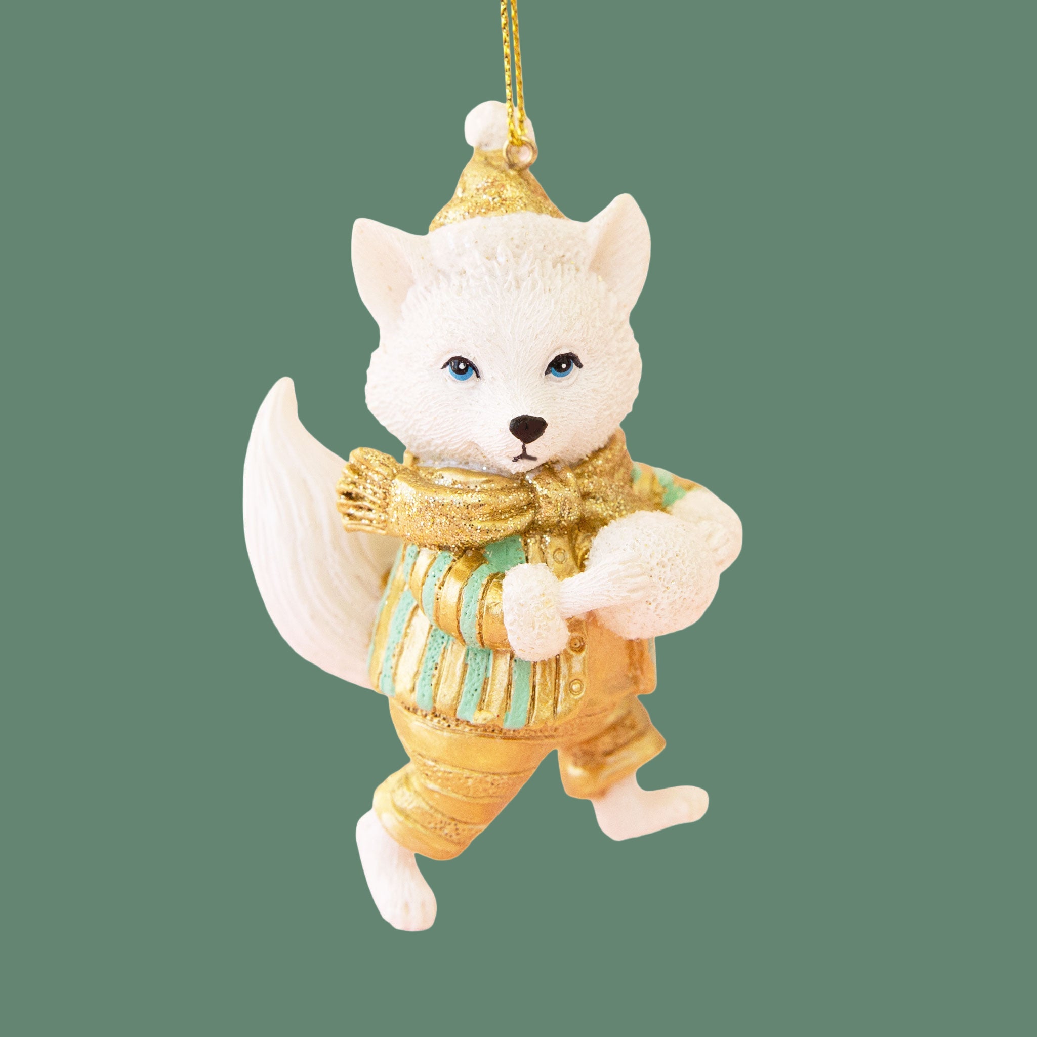 Fox ornament with white fur, gold clothes, and teal accents. The fox is holding a snowball. 
